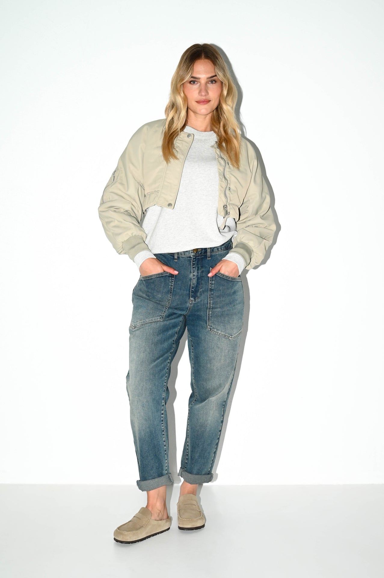 dame poseert met handen in zakken van een grijsblauwe carrot fit spijkerbroek met comfortabele pasvorm en used denim wassing